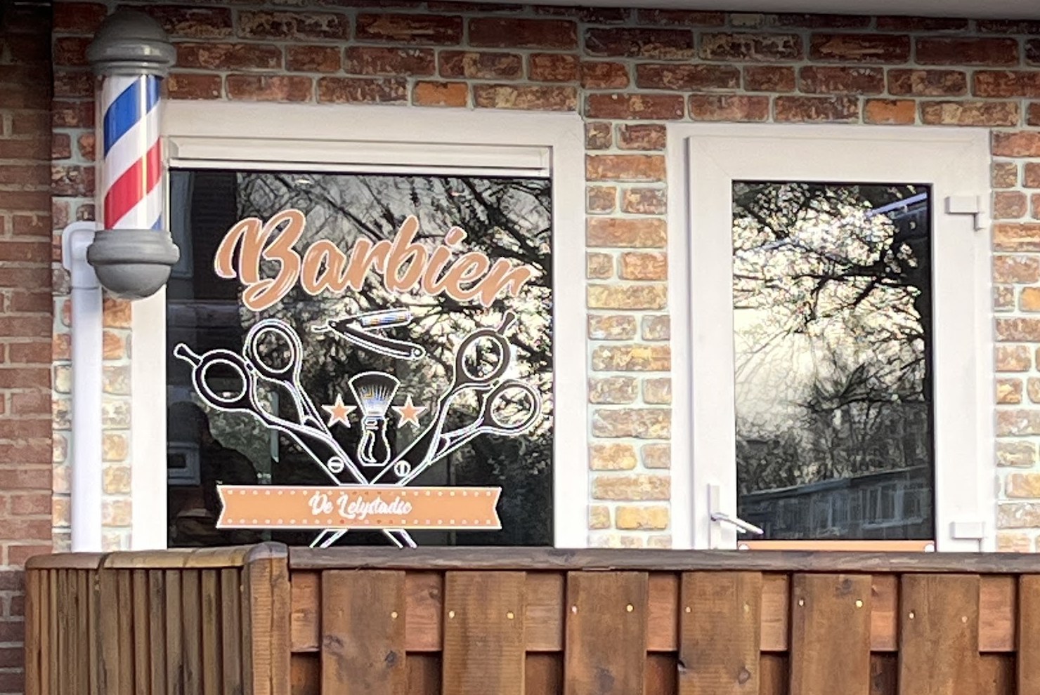 De etalage met de koperen Barbier-belettering en de barberpaal naast de deur